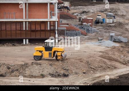 Apripista che costruisce e costruisce una nuova strada asfaltata nei pressi di edifici civili. Concetti di miglioramento del territorio degli edifici. Foto Stock