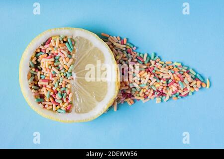 Una fetta di limone piena di polpa e dolci lascia una traccia di caramelle colorate su uno sfondo blu pastello. Zucchero e frutta nei dessert. Foto Stock