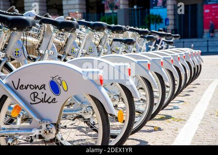 VERONA, ITALIA - 18 agosto 2020: Una fila di biciclette elettriche fotografate da dietro al sole nella città di Verona in affitto ai turisti. Sulle biciclette Foto Stock