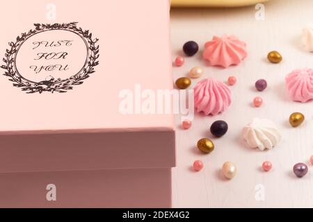 confezione regalo rosa con dolci multicolore sparsi e torta bizet su un tavolo di legno bianco Foto Stock