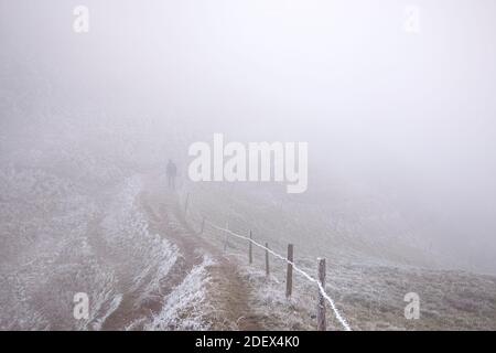 Uomo che cammina nella nebbia. Paesaggio invernale con figura sul sentiero escursionistico su sentiero in montagna a temperatura fredda. Concetto Wanderer. Foto Stock