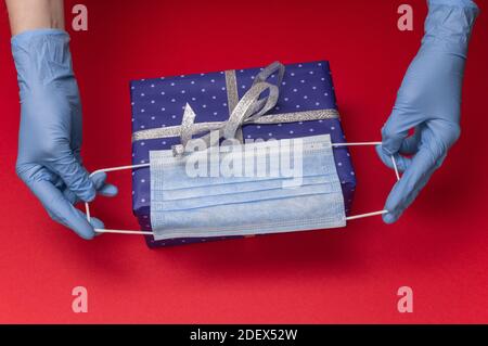 Mani in guanti blu in lattice contiene scatola regalo blu in carta con pois di polka con nastro legato con come regalo per Natale, Capodanno, giorno di San Valentino Foto Stock