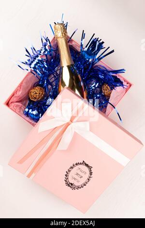 una bottiglia d'oro di champagne si trova in un regalo rosa Scatola con un arco e una tindel di Natale blu su un sfondo bianco della tabella Foto Stock