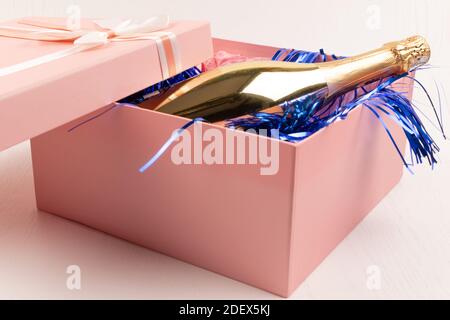 una bottiglia d'oro di champagne si trova in un regalo rosa Scatola con un arco e una tindel di Natale blu su un sfondo bianco della tabella Foto Stock