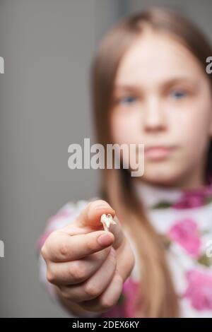 Ragazza di età elementare che mostra il dente del bambino estratto con carie in clinica dentale - concetto di igiene orale difettoso. Mettere a fuoco su un dente Foto Stock