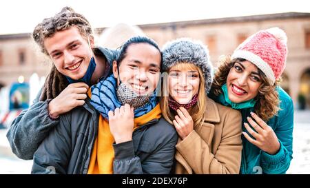 Amici multiculturali che prendono felice selfie indossando maschera facciale e inverno Vestiti - nuovo concetto di stile di vita normale con la gente milenial che ha divertimento insieme Foto Stock