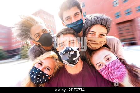 Amici multirazziali che prendono selfie con maschere facciali - amicizia felice concetto con i giovani studenti che si divertono insieme dopo la riapertura dell'università Foto Stock