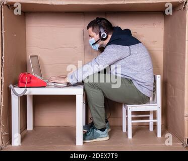 il dipendente lavora dal proprio ufficio di cartone per isolarsi da altri Foto Stock