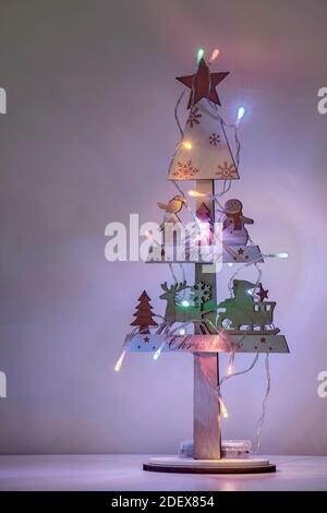 Albero di Natale in miniatura di legno decorato con Babbo Natale e un pupazzo di neve, illuminato con luci colorate con uno sfondo sfocato Foto Stock