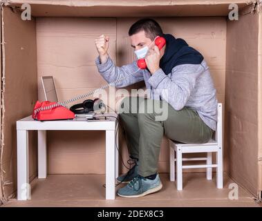 il dipendente lavora dal proprio ufficio di cartone per isolarsi da altri Foto Stock