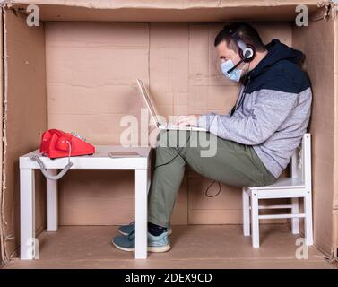 il dipendente lavora dal proprio ufficio di cartone per isolarsi da altri Foto Stock