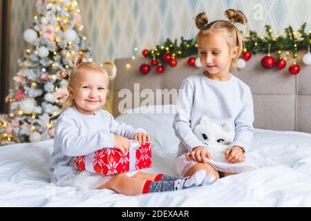 Due sorelle carine delle ragazze con i regali di Natale siedono sul letto A casa in camera decorata a Natale Foto Stock
