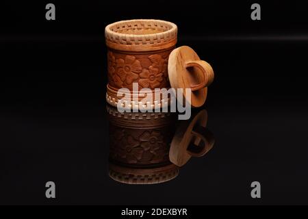 Un tradizionale caschetto russo fatto di corteccia di betulla con motivo floreale si erge su vetro nero, in cui il suo riflesso è visibile. Foto Stock