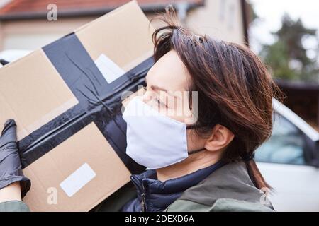 Servizio di consegna il gestore pacchi con maschera porta il pacco per la consegna Foto Stock