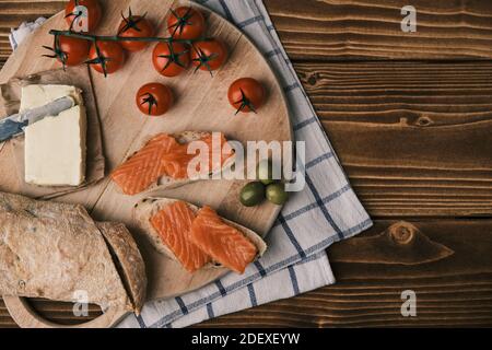 Due panini con salmone affumicato e altro cibo sulla vecchia tavola su rustico sfondo di legno. Vista dall'alto Foto Stock