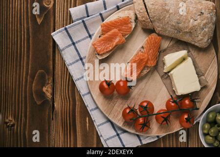 Due panini con salmone affumicato e altro cibo sulla vecchia tavola su rustico sfondo di legno. Vista dall'alto Foto Stock