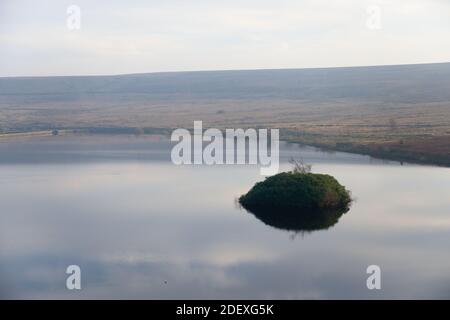 Serbatoio centrale di Redmires serbatoi in un pomeriggio tranquillo, che riflette un cielo blu chiaro. Piccola isola di piante sopravuta si staglia al buio sopra l'acqua Foto Stock