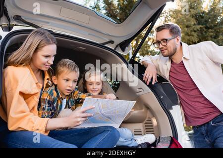 Sorridente famiglia che guarda la mappa vicino al bagagliaio dell'auto durante vacanza Foto Stock