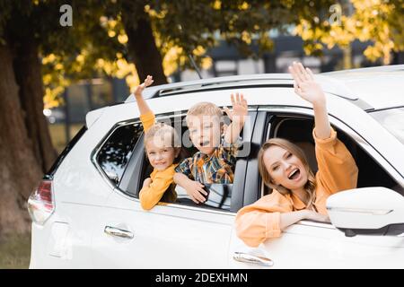 Sorridi i bambini che agitavano le mani vicino alla madre durante il viaggio in auto Foto Stock