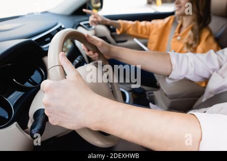 Vista ritagliata dell'uomo che guida l'auto vicino a moglie che indica con dito su sfondo sfocato Foto Stock