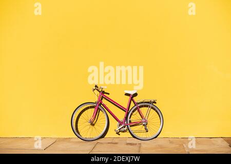 bici rosa retro supportata su una parete colorata gialla, concetto di stile di vita attivo e mobilità urbana sostenibile, spazio di copia per il testo Foto Stock