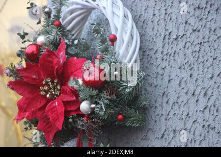 Corona di Natale con elementi decorativi e baubles appesi su parete grigia. Foto Stock