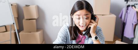Eccitato volontario asiatico che parla al telefono con centro di beneficenza offuscato sullo sfondo, banner Foto Stock