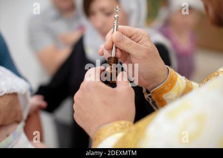 Le mani del sacerdote tengono una bottiglia di incenso e un pennello per il battesimo. Foto Stock