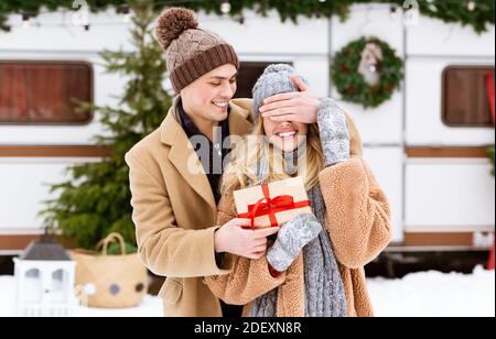 Sorpresa di Natale. Amore giovane Guy che copre gli occhi della ragazza all'aperto e dare presente Foto Stock