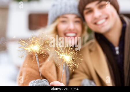 Sparklers brucianti nelle mani di giovane coppia romantica invernale in piedi All'aperto Foto Stock