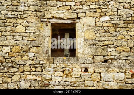 Gesù sulla croce, antico crocifisso, visibile dall'esterno, posto nella piccola finestra al centro della facciata medievale. Dordogna, a sud-ovest della Francia. Foto Stock