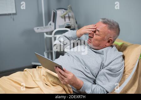 Un uomo anziano con una linguetta digitale tra le mani che gli strofina gli occhi stanchi. Foto Stock