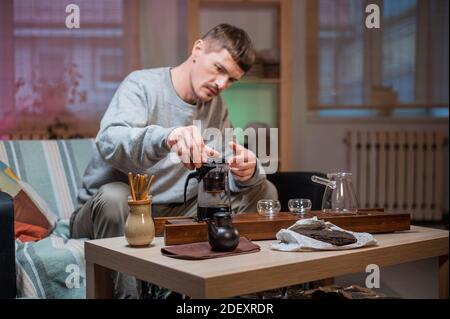 Un uomo attende gli ospiti e prepara un autentico tè cinese utilizzando un kit per la cerimonia del tè. Eroga le foglie di tè crudo mature in acqua calda secondo le istruzioni del maestro del tè Foto Stock