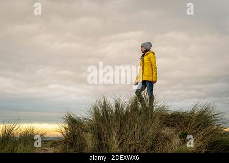 Donna che indossa un cappotto giallo in piedi sulla cima di una duna, concetto di copertina del libro. Foto Stock