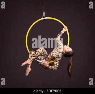 Una giovane donna in tuta con stampa esegue elementi acrobatici nell'anello dell'aria. Riprese in studio su sfondo nero. Foto Stock