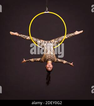 Una giovane donna in tuta con stampa esegue elementi acrobatici nell'anello dell'aria. Riprese in studio su sfondo nero. Foto Stock
