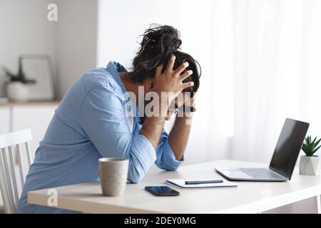 Problemi di lavoro. Millennial Freelancer Guy Siting alla scrivania e toccando testa nella disperazione Foto Stock