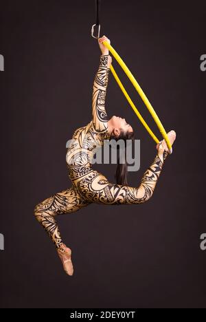 Una giovane donna in tuta con stampa esegue elementi acrobatici nell'anello dell'aria. Riprese in studio su sfondo nero. Foto Stock