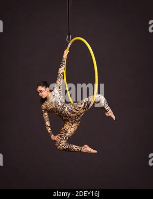 Una giovane donna in tuta con stampa esegue elementi acrobatici nell'anello dell'aria. Riprese in studio su sfondo nero. Foto Stock