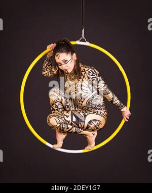Una giovane donna in tuta con stampa esegue elementi acrobatici nell'anello dell'aria. Riprese in studio su sfondo nero. Foto Stock