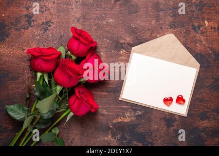 Biglietto d'auguri per San Valentino fiori di rosa rossa bouquet e artigianato Busta con cuori rossi su fondo di legno vintage piatto Vista dall'alto - immagine Foto Stock