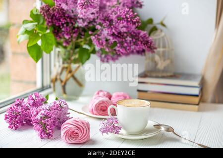 Bouquet di lilacs, tazza di caffè, marshmallow fatto in casa e pila di libri. Romantica mattina di primavera. Messa a fuoco selettiva Foto Stock