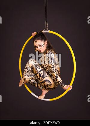 Una giovane donna in tuta con stampa esegue elementi acrobatici nell'anello dell'aria. Riprese in studio su sfondo nero. Foto Stock