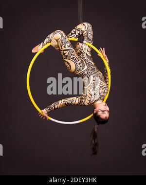 Una giovane donna in tuta con stampa esegue elementi acrobatici nell'anello dell'aria. Riprese in studio su sfondo nero. Foto Stock