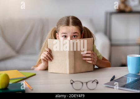 Ragazza spaventata con gli occhi aperti che si nascondono dietro un libro Foto Stock