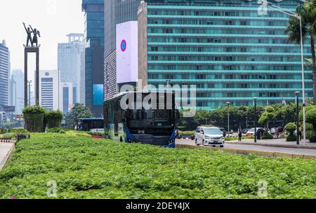 Giacarta / Indonesia - 25 ottobre 2020. Un autobus blu transjakarta che attraversa l'area della rotatoria indonesiana dell'hotel sullo sfondo di grattacieli Foto Stock