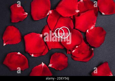 Due anelli di nozze in argento su petali di rosa rossa Foto Stock