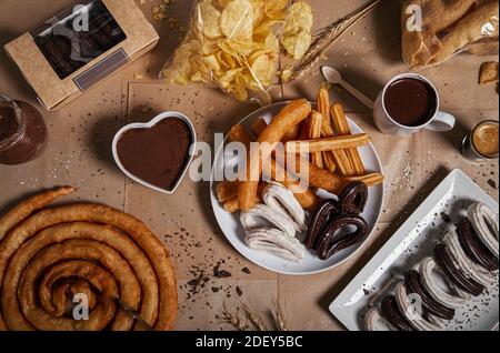 Varietà di churros tradizionali con zucchero granulato e cioccolato su fondo di carta craf. Vista dall'alto con spazio per la copia. Prodotti tipici della churreria Foto Stock