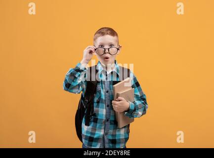 Schooler sorpreso con occhiali che tengono libri su sfondo giallo Foto Stock