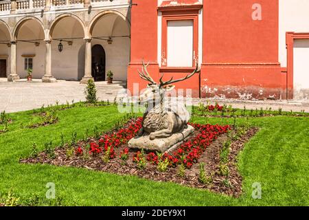 Opochno, Repubblica Ceca - Giugno 16 2020: Vista della statua del cervo nel mezzo del letto di fiori e prato verde posto sul cortile del castello con portici. Foto Stock